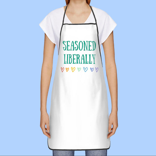 Person wearing a white apron with 'Seasoned Liberally' text and colorful hearts on a white background